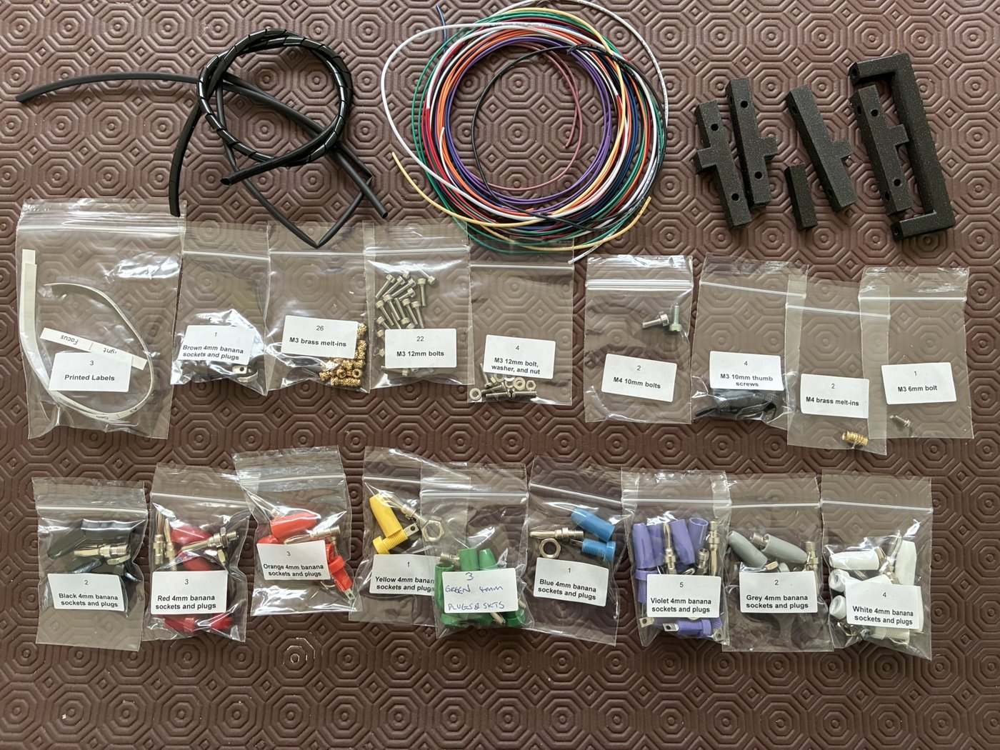 Figure 2 — The acrylic case kit: laser-cut clear panels (5 mm or 6.35 mm), 3D-printed corner posts, a handle, corner thumb screws, and the M3 hardware, jacks, wire, and heat-shrink that finish the box. The pa…